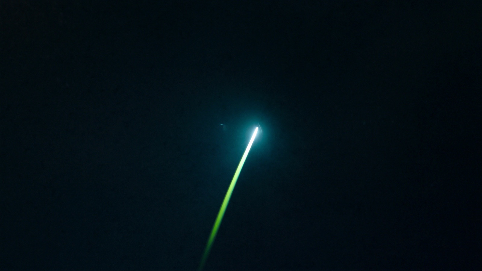 A launch vehicle ascending on a chartreuse-lit exhaust trail into a dark sky
