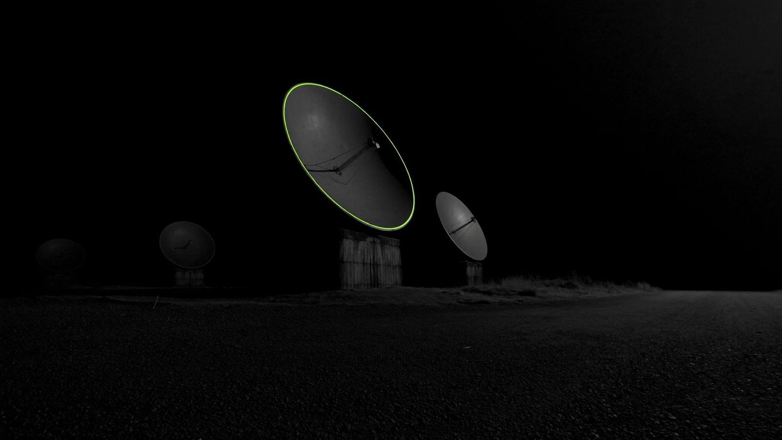 A row of large parabolic teleport antennas on a dark moorland at night, one chartreuse rim-light tracing the largest dish